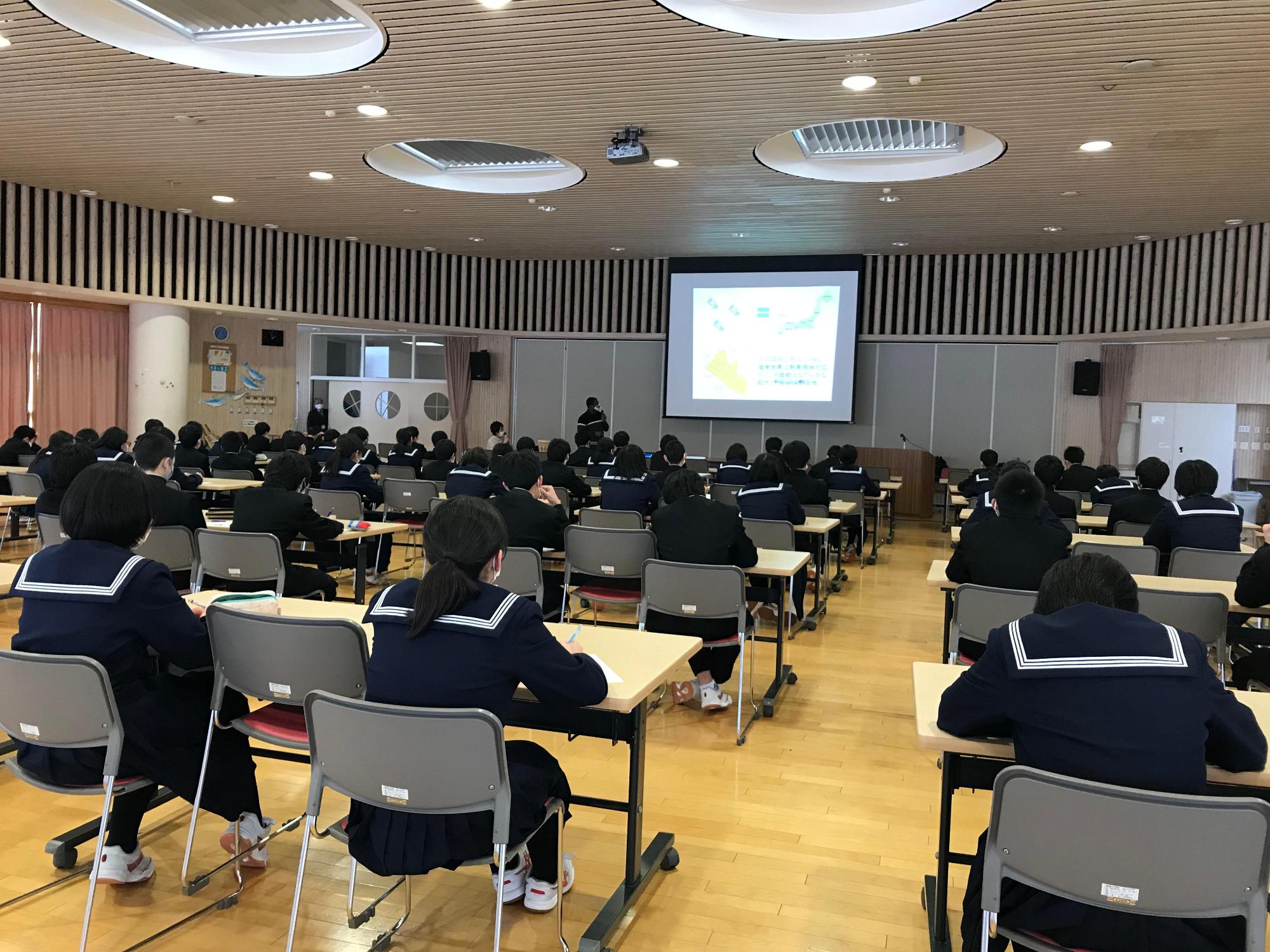 後方より撮影された、リベリア講座の実施風景の写真。生徒たちが各自長机の席からスティーブンス・モール氏の話を聞く様子が確認できる