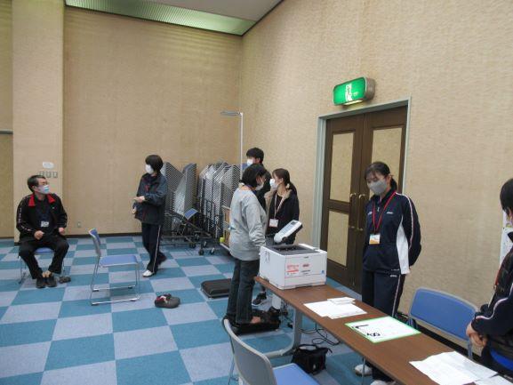 会議室の壁際で、実技前の測定として体重測定を受ける参加者の写真