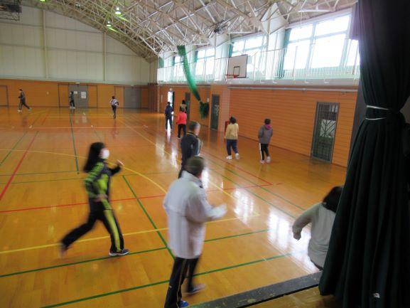 体育館のステージ上より俯瞰で撮影された、早歩きでステージ手前を通過する参加者たちの写真