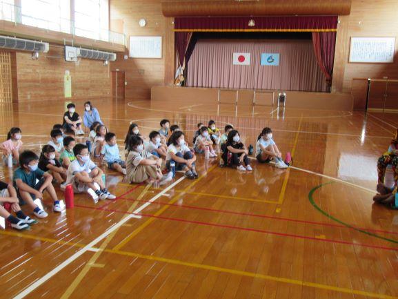 リベリア講座に臨んで、体育館の床に座って話を聞く児童たちの写真