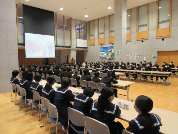 食堂の隅から撮影された、リベリア講座風景のほぼ全景写真。食堂にはスライドショー用のスクリーンも展開されており、並べられた長机の席から講演を聞く生徒たちの様子が確認できる