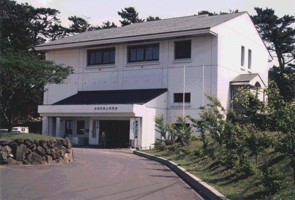 低木や木々に囲まれた白い郷土資料館の外観の写真