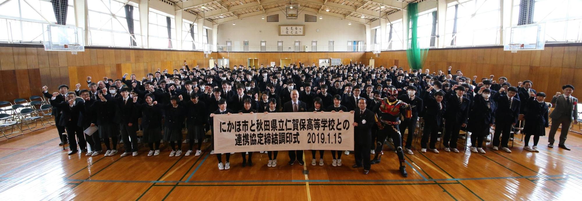 制服姿の学生たちと教員が体育館で一堂に会する写真