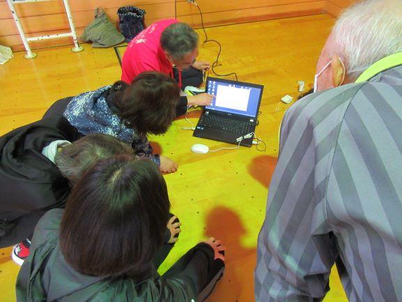 体育館の隅に座り、実技で計測されたデータをノートPCで確認する参加者たちとインストラクターの写真