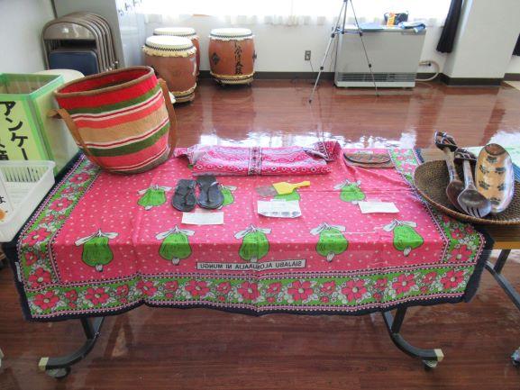 リベリア講座にて展示されたリベリアの生活道具の写真。カラフルな布が巻かれた籠やサンダル、食器等が卓上に陳列されている