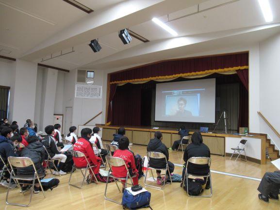 象潟公民館におけるオンライン講演会の実施風景の写真。舞台上のスクリーンにはオンラインで臨む上原氏の画面が映し出されている