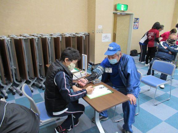 会議室の隅で、実技前の体調チェックとして血圧測定を受ける参加者の写真
