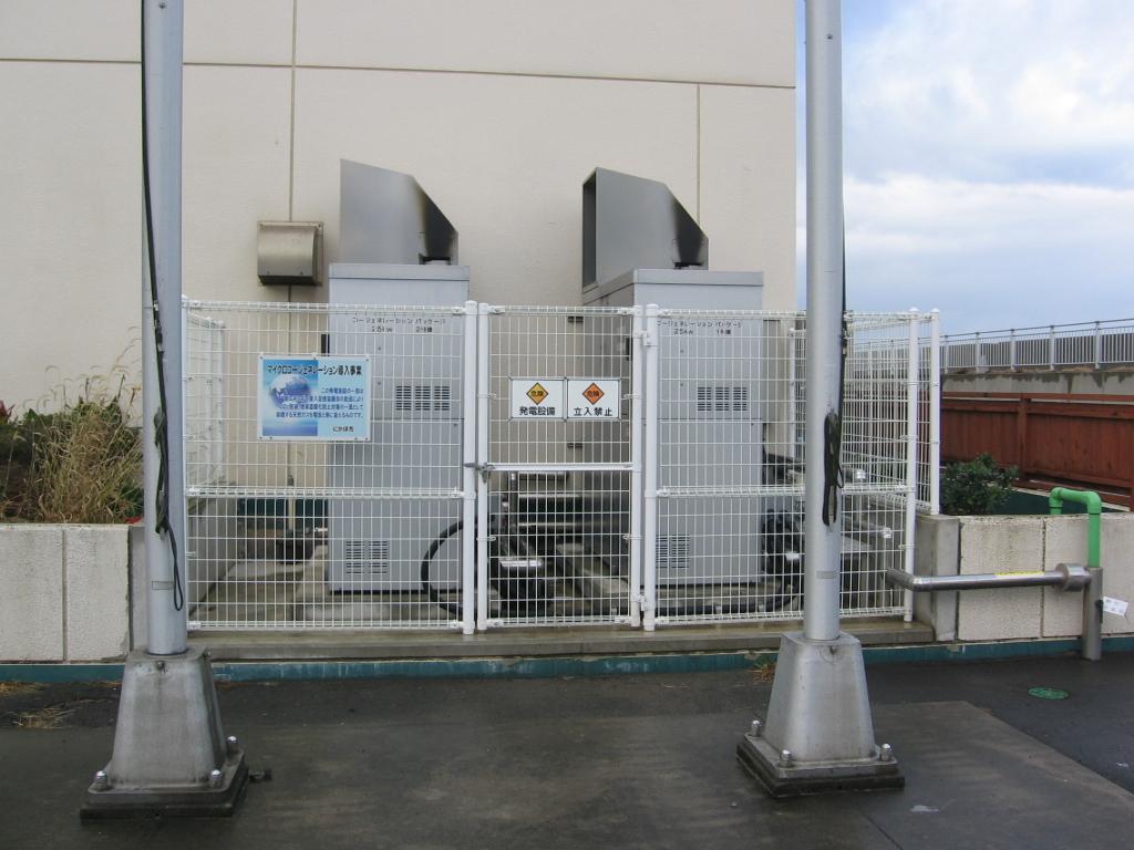 二本の柱の後ろにフェンスで囲まれた発電設備がある写真