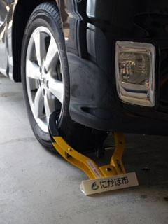 四輪自動車の前輪に施された、タイヤロックの措置例の写真。ロックした器具には「にかほ市」と書かれた文字とにかほ市市章が確認できる