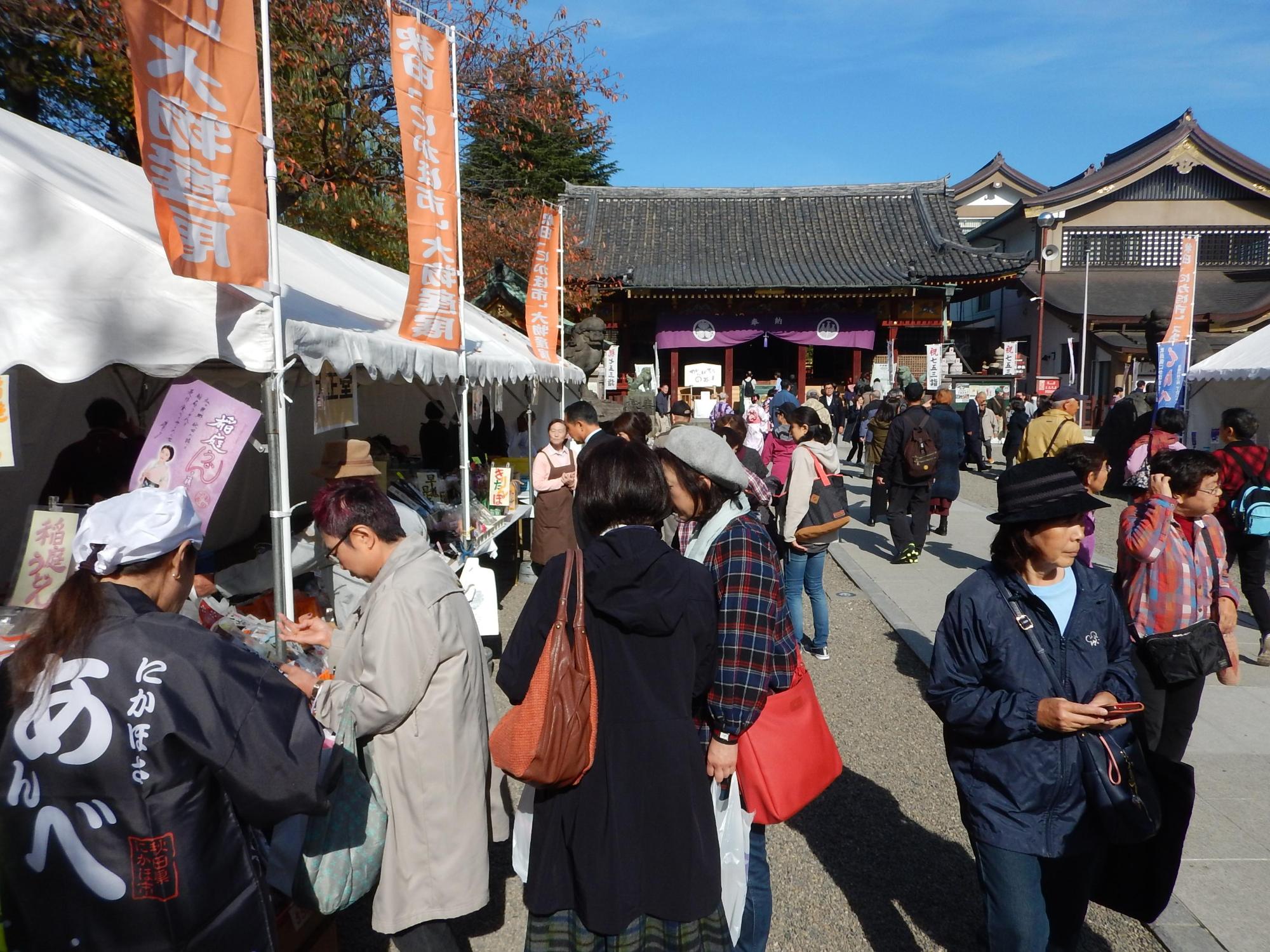 神社の入口に多数の屋台が並んでいて人々が買い物をしている写真