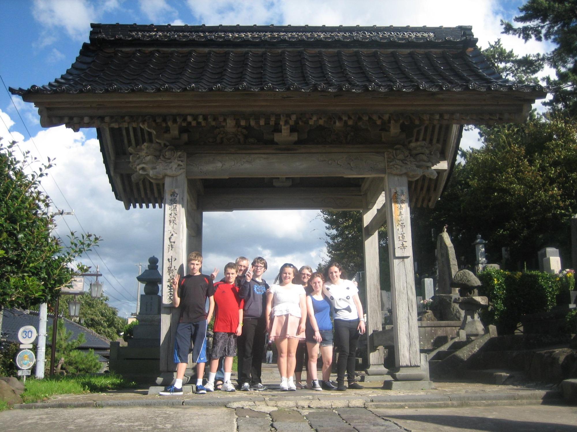 青空の下、山門の前で8名の外国人達が横一列に並んだ集合写真